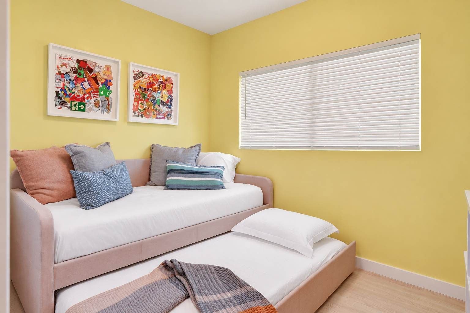 A bedroom with a bed, pillows, a blanket, and two framed artworks on the wall.