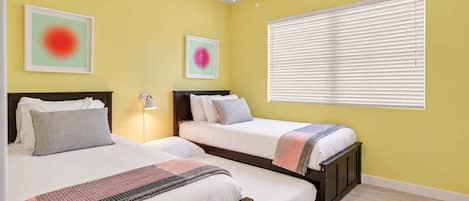A hotel room with two beds, a ceiling fan, a window with blinds, and artwork on the walls.
