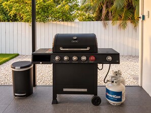 A black outdoor grill with a side table, a trash can, and a propane tank. - Hot-Tub, Pool, Basketball, Fire Pit, Pong | Casa (Miami)