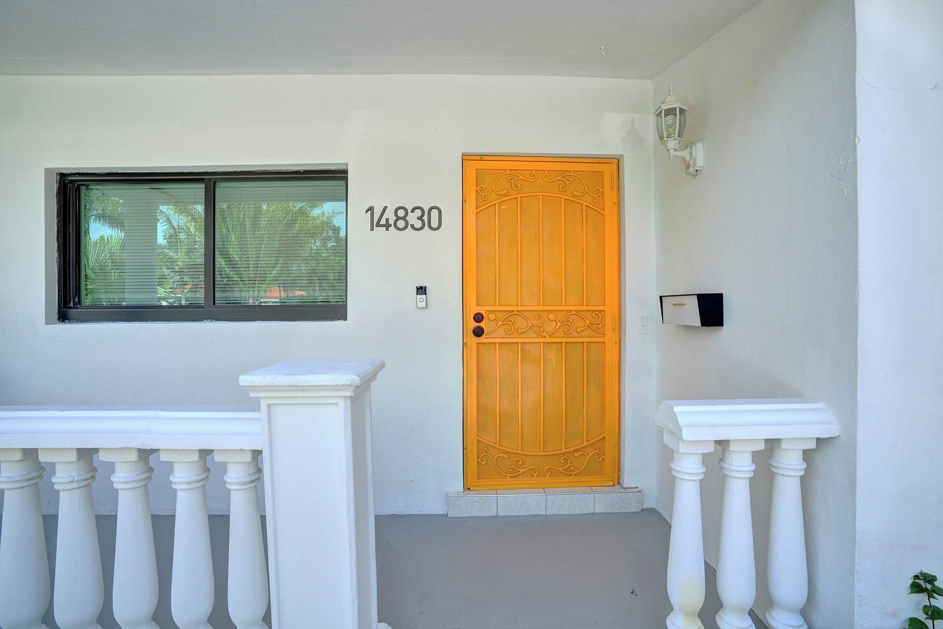 Un edificio blanco con el número '14830' sobre una puerta de madera, una ventana con persianas y una barandilla blanca.