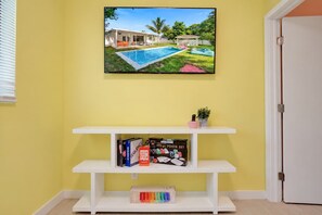 A room with a white entertainment center, a framed picture of a pool, and a door. - Hot-Tub, Pool, Basketball, Fire Pit, Pong | Casa (Miami)