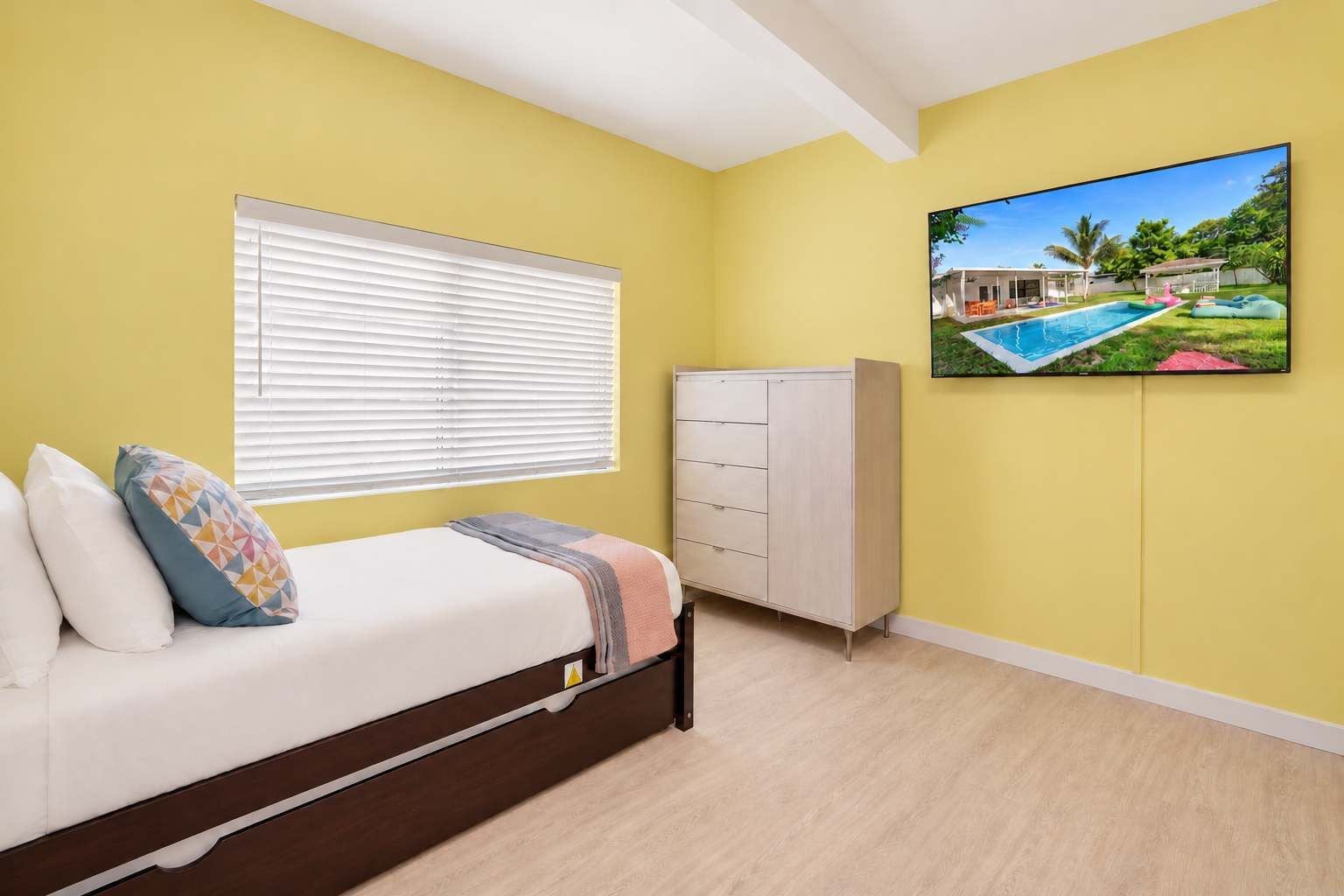 Un dormitorio con cama, cómoda, ventana con persianas y un cuadro de una casa en la pared.