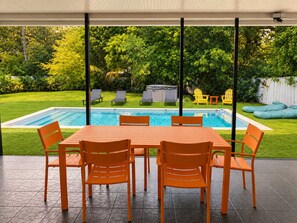 An outdoor patio with a pool, surrounded by greenery and a white fence. - Hot-Tub, Pool, Basketball, Fire Pit, Pong | Casa (Miami)