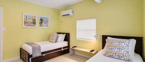 A bedroom with two beds, a bedside table, a lamp, and wall art.
