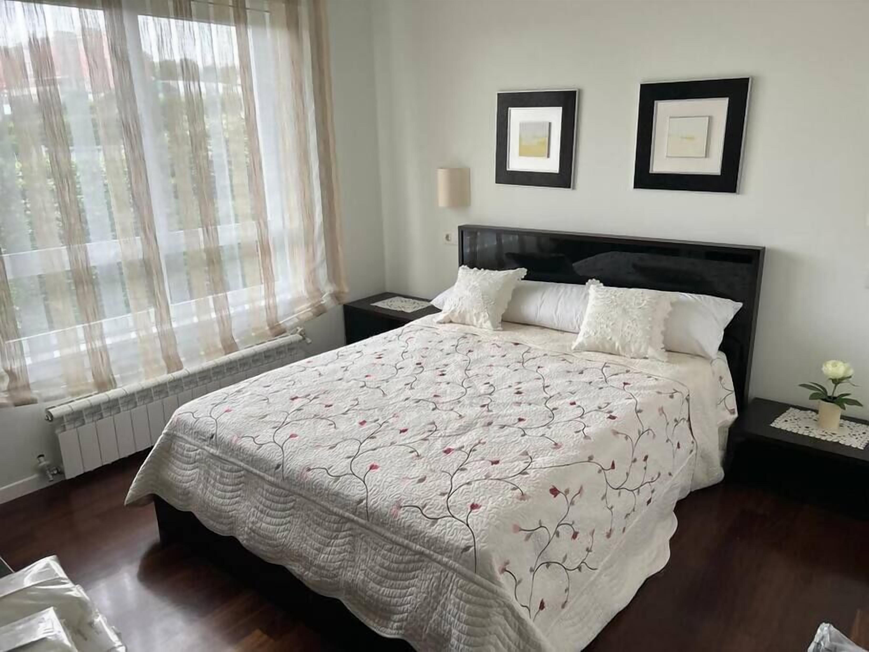 A neatly made bed with a floral-patterned bedspread, two bedside tables with lamps, and two framed pictures on the wall.