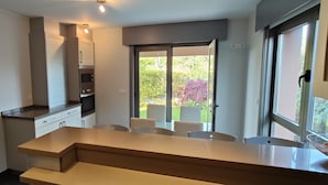 A modern kitchen with built-in appliances, a dining area with chairs, and a sliding glass door leading to a garden. - Excepcional Chalet en Perbes (Perbes (San Pedro))