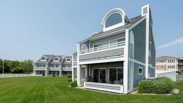 A modern two-story house with a large front porch, a covered patio, and a well-maintained lawn. - Waterfront Condo in Spring Lake-Blissful Blue Waterfront (Spring Lake)