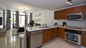 A modern kitchen with stainless steel appliances, wooden cabinets, and a large island with a sink. - Lovely apt in the heart Midtown (Miami)
