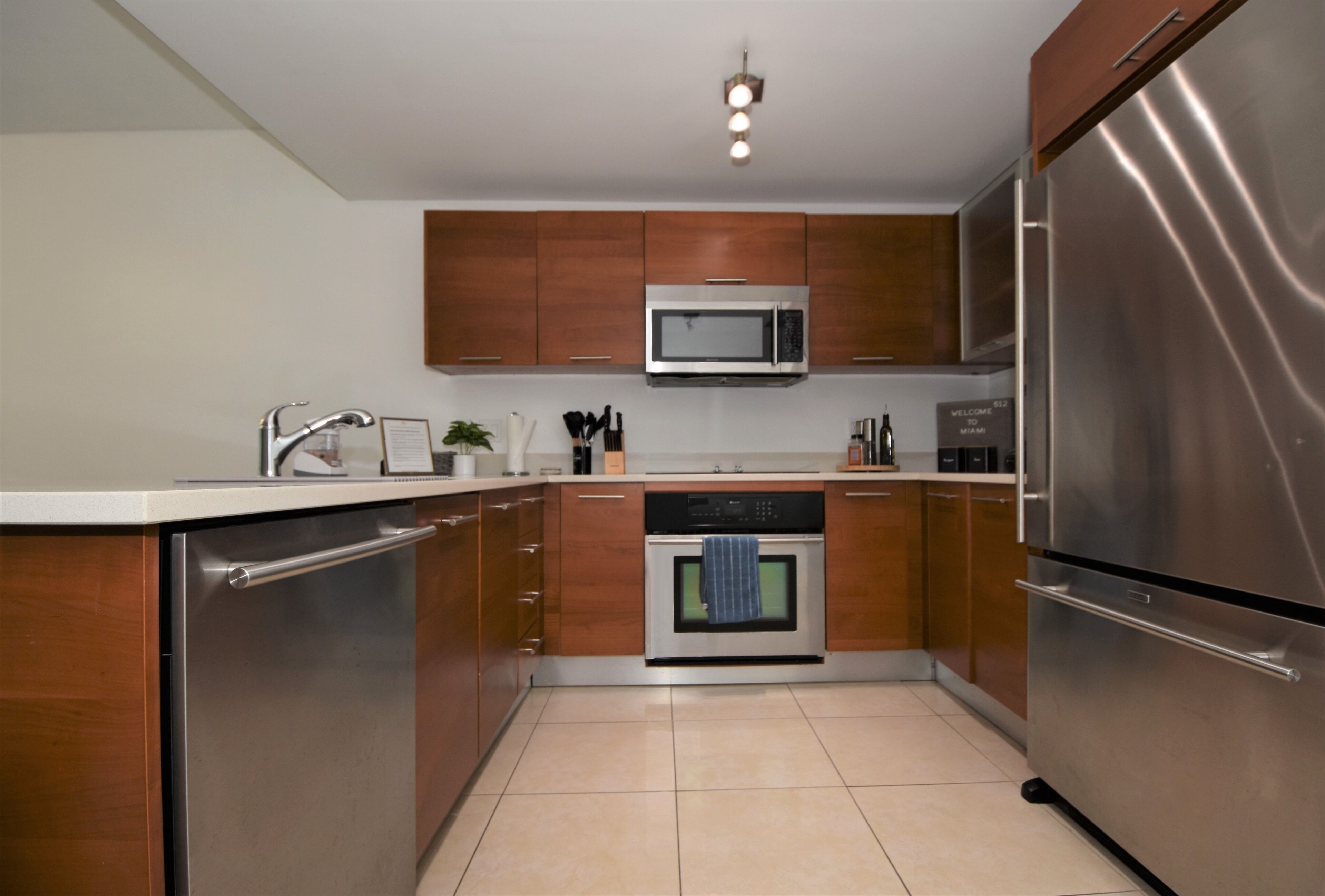 A modern kitchen with stainless steel appliances, wooden cabinets, and a tiled floor.