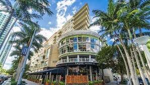 A modern hotel with a curved facade, outdoor seating area, and palm trees. - Lovely apt in the heart Midtown (Miami)
