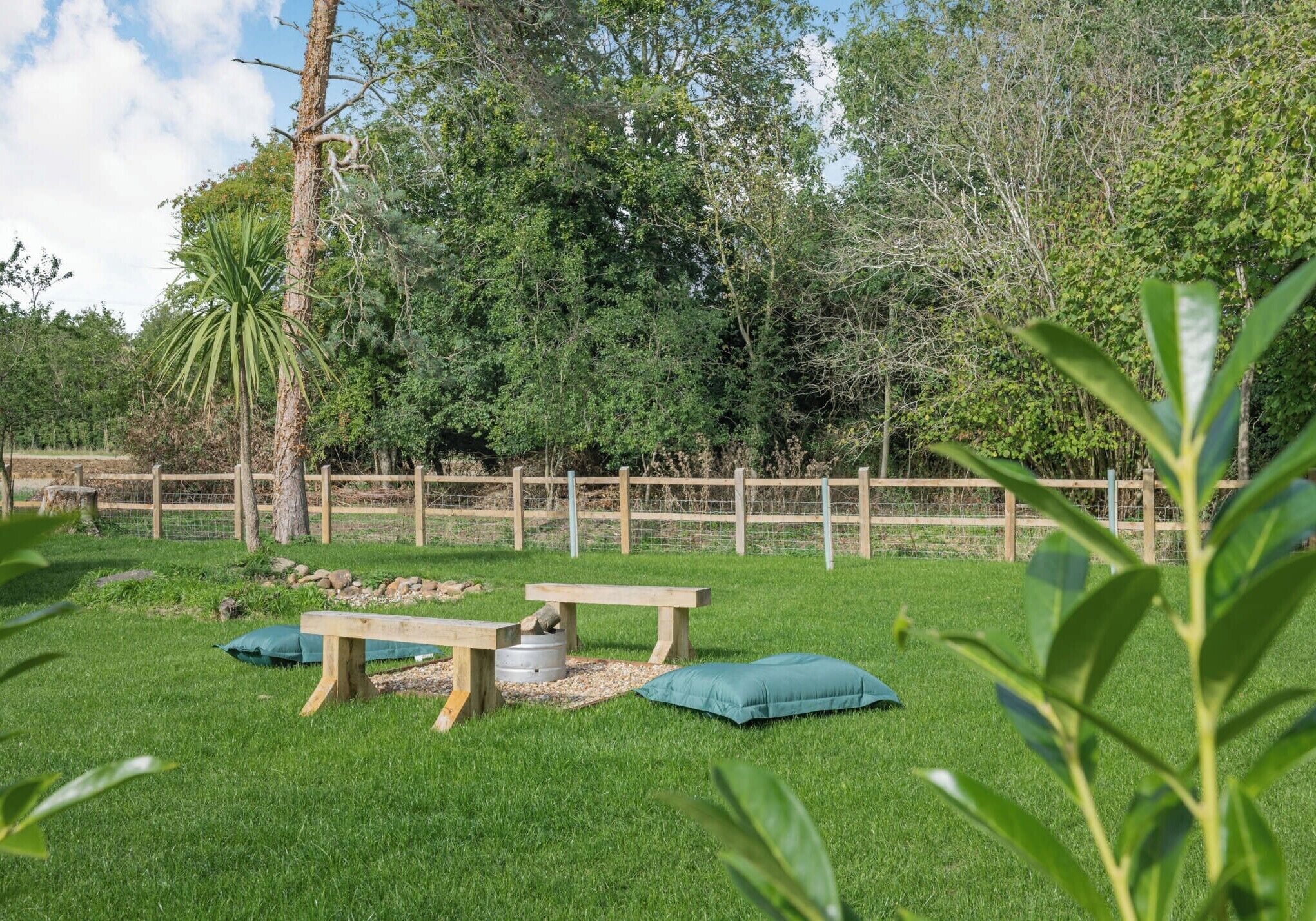 A grassy outdoor area with a wooden fence, a bench, and a table with a cushion.