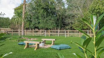 A grassy outdoor area with a wooden fence, a bench, and a table with a cushion.