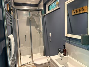A bathroom with a glass-enclosed shower, a white sink, and a mirror with a wooden shelf.