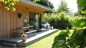 En træbygning med en overdækket terrasse, et bord, stole og en potteplante.