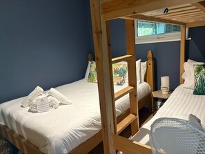 A room with two wooden bunk beds, a small table with a cup, and a window with blinds.