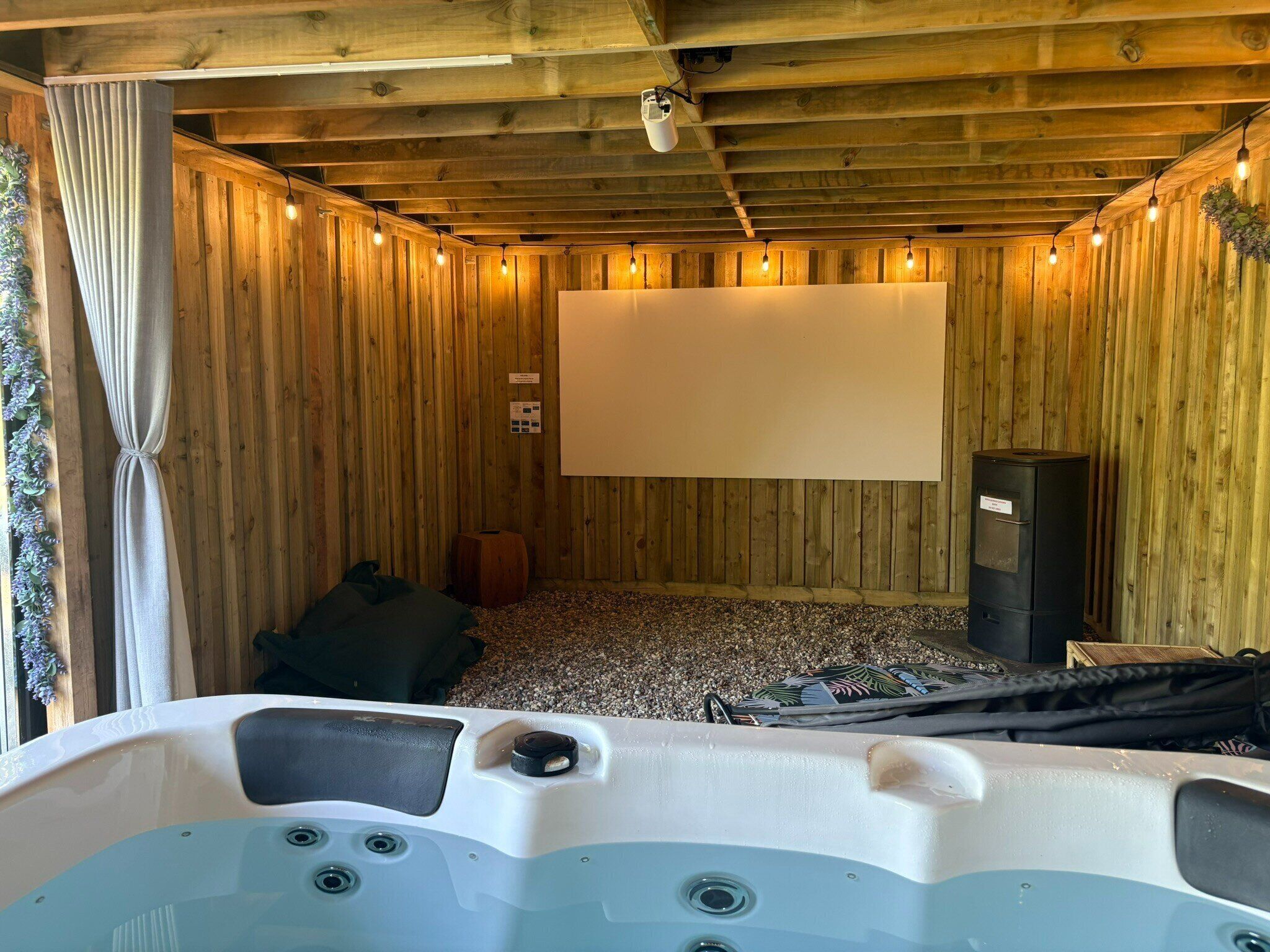Una habitación de madera con un jacuzzi, una pantalla de proyector y un altavoz.