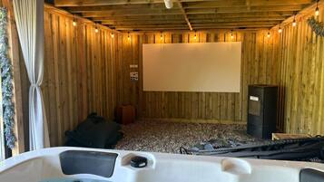 Una habitación de madera con un jacuzzi, una pantalla de proyector y un altavoz.