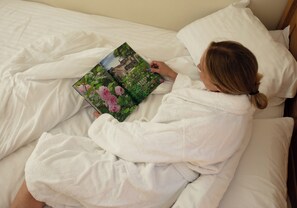 A person lying in bed reading a book. - Woodland lodge with hot tub, cinema area, sauna access & enclosed garden — ideal for couples (Halstead)