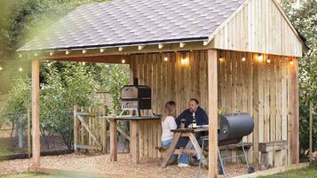 A wooden outdoor structure with a pitched roof, a barbecue grill, and string lights.