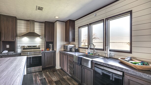 A modern kitchen with dark wood cabinets, stainless steel appliances, and a large window providing natural light. - ‘Sunset Cove’ Lakefront Rental w/ Private Dock! (Onalaska)