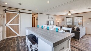 A kitchen with a wooden barn-style door, a central island with chairs, a dining table, and a ceiling fan. - ‘Sunset Cove’ Lakefront Rental w/ Private Dock! (Onalaska)
