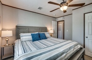 Un letto rifatto con cura, lenzuola a righe e due cuscini, una ventola a soffitto e lampade sui comodini.