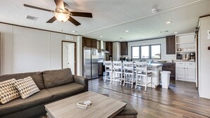 A modern kitchen with white cabinets, a stainless steel refrigerator, and a dining area with white chairs. - ‘Sunset Cove’ Lakefront Rental w/ Private Dock! (Onalaska)