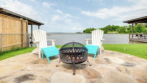 A stone patio with a fire pit and two Adirondack chairs facing a lake. - ‘Sunset Cove’ Lakefront Rental w/ Private Dock! (Onalaska)