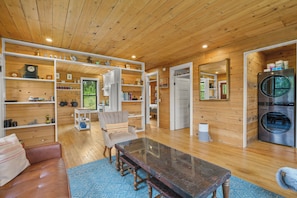 Een houten interieur met een eettafel, bank en planken met diverse spullen.