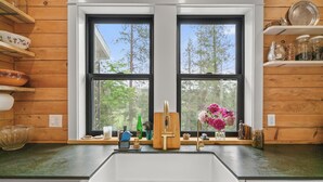 Cocina con pileta doble, estantes de madera y ventana con vista a los árboles.