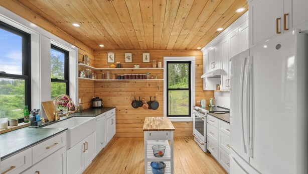 Una cocina moderna con paredes de madera, armarios blancos y un amplio ventanal.
