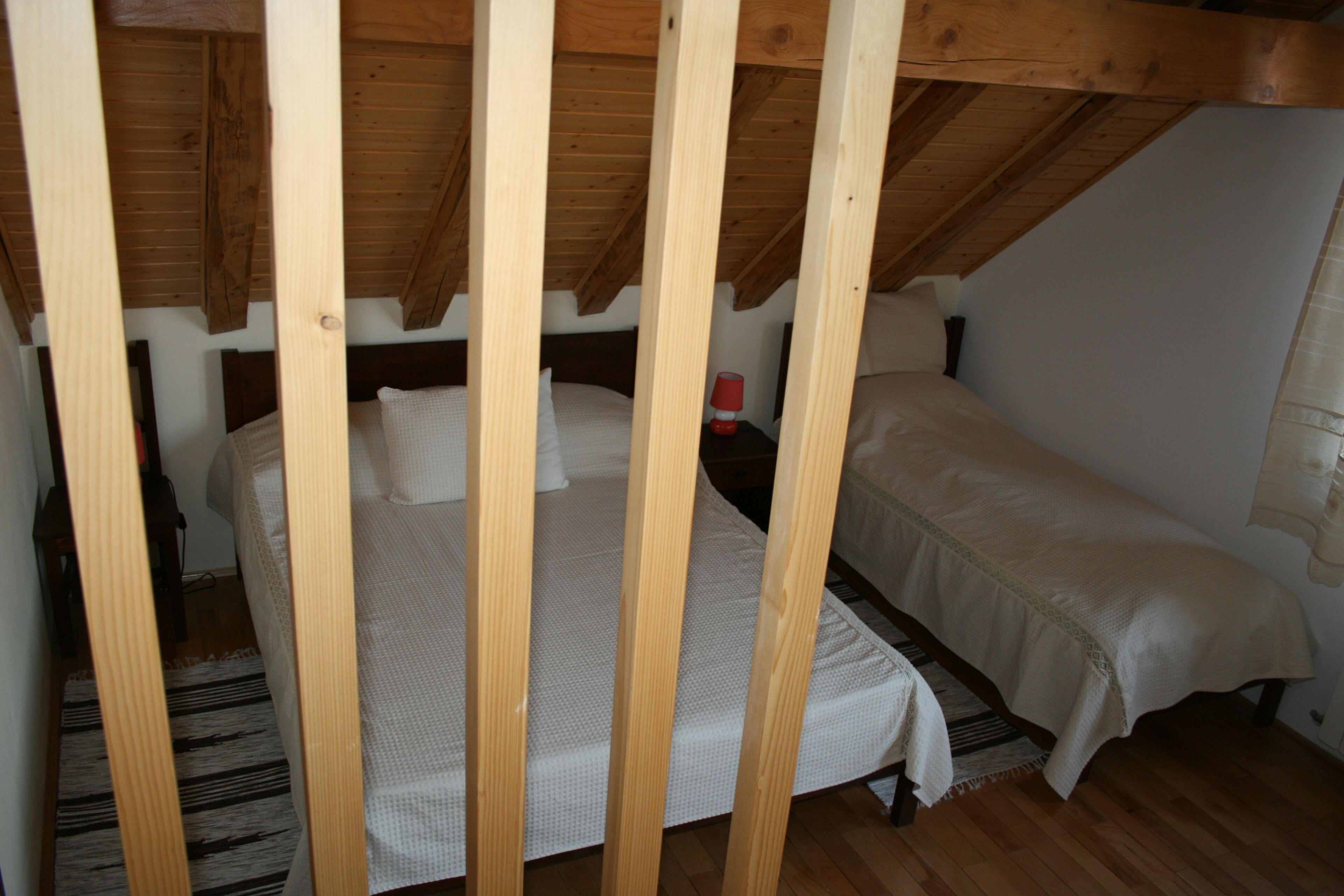 Une chambre avec deux lits, des poutres en bois, un tapis à rayures et une table de chevet avec une lampe rouge.