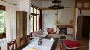 Uma sala de jantar com uma mesa comprida, cadeiras, um vaso com flores e uma cesta de frutas.