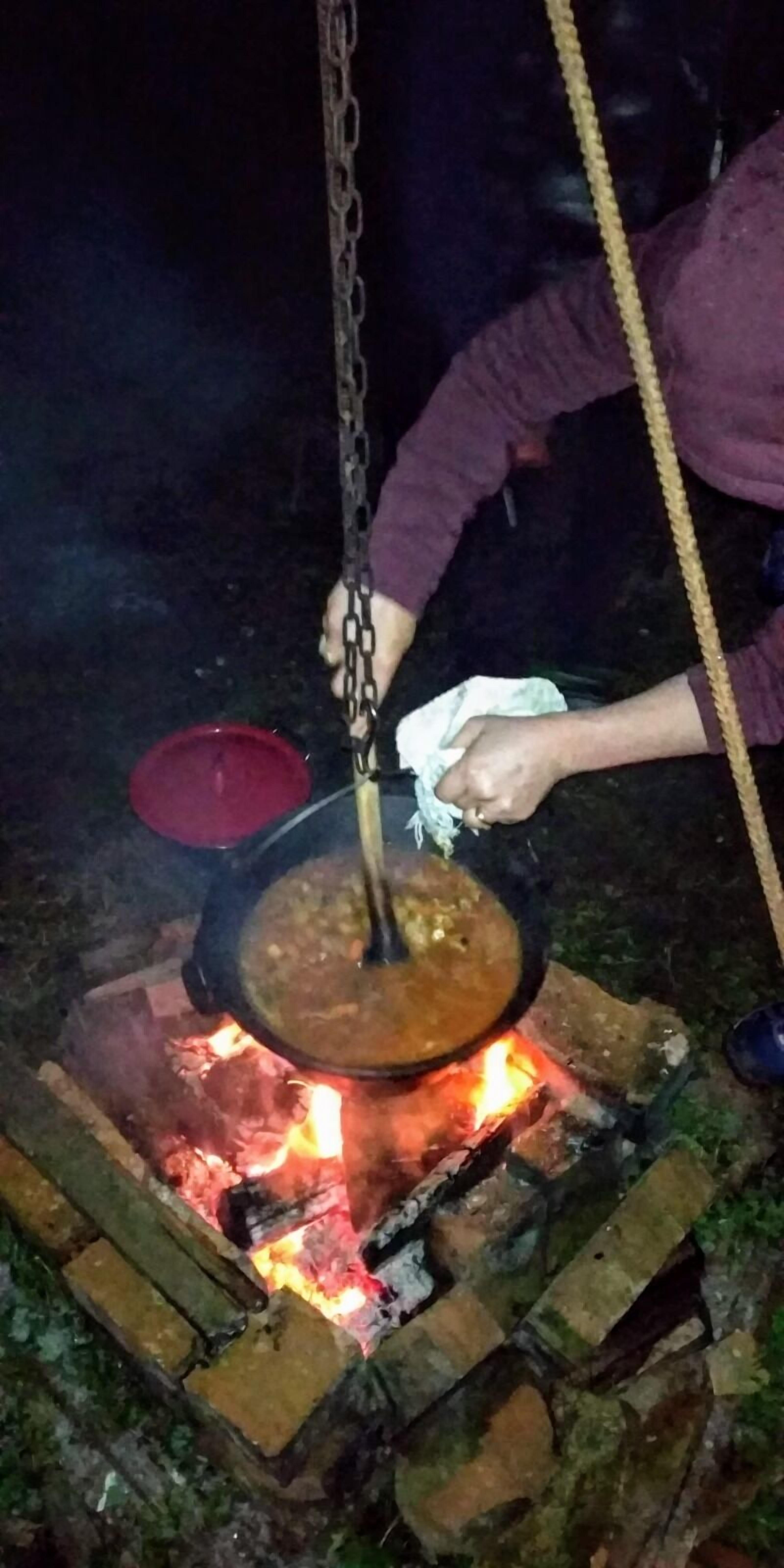Iemand kookt boven een open vuur met een pan.