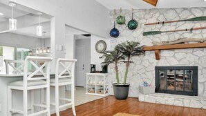 A modern living room with a stone fireplace, white bar stools, a potted plant, and decorative items on the wall. - 1 Mi to Beach: Charming Largo Home w/ Private Pool (Largo)
