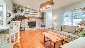 A living room with a stone fireplace, wooden furniture, and a view of the outdoors through large windows. - 1 Mi to Beach: Charming Largo Home w/ Private Pool (Largo)