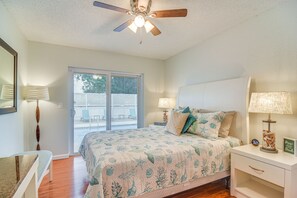 Une chambre à coucher avec un lit, des tables de chevet, un ventilateur de plafond et une vue sur l’extérieur.