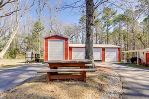 Un edificio rojo con dos puertas de garaje, una mesa de picnic al frente y un árbol cercano.