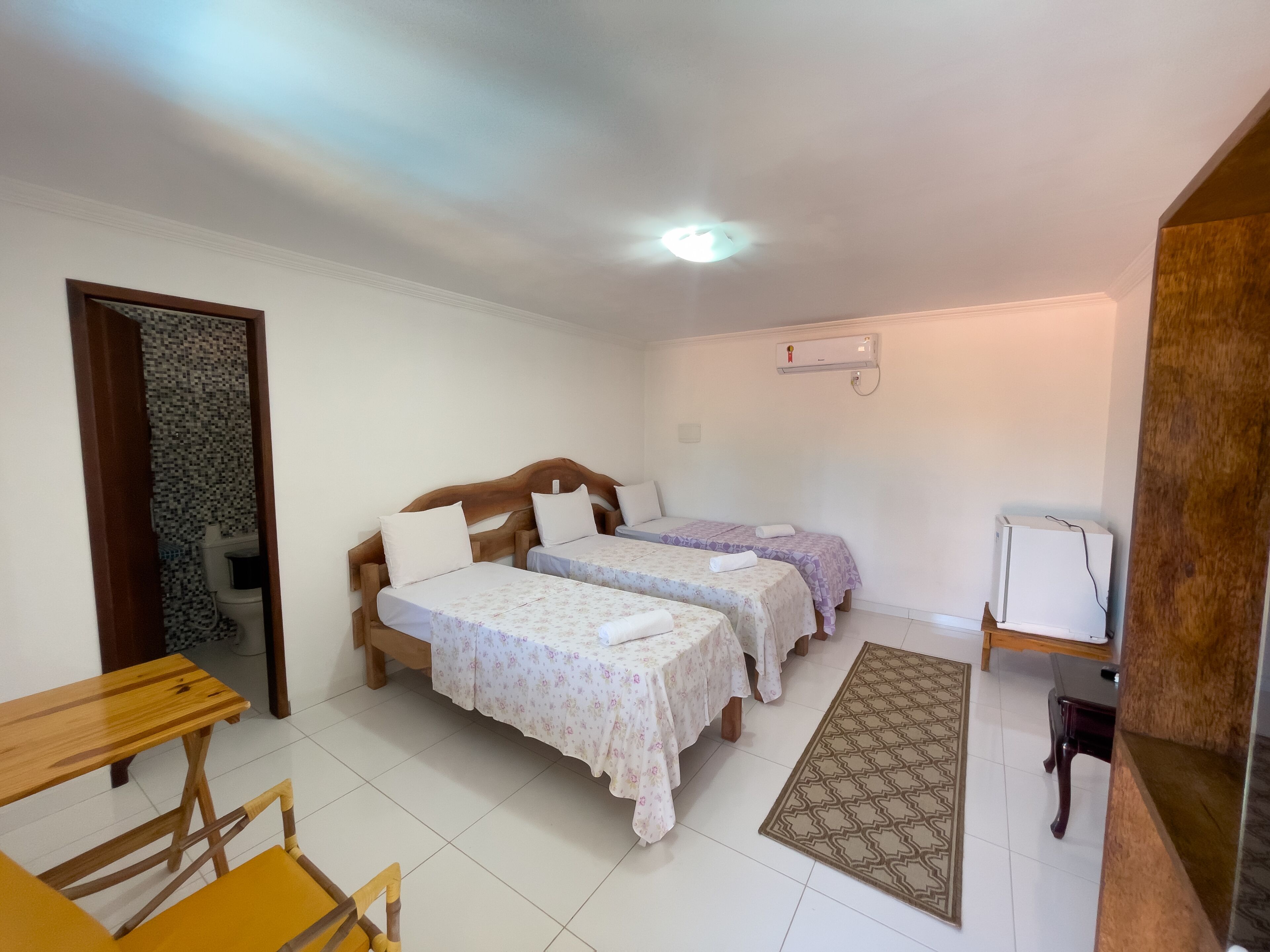 A room with two wooden beds, a small table, a chair, a patterned rug, and a white refrigerator.