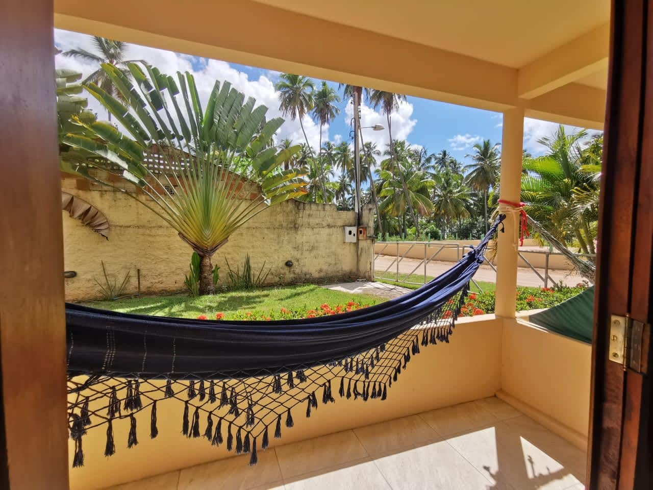 Una hamaca en un balcón con vista a palmeras y un jardín.