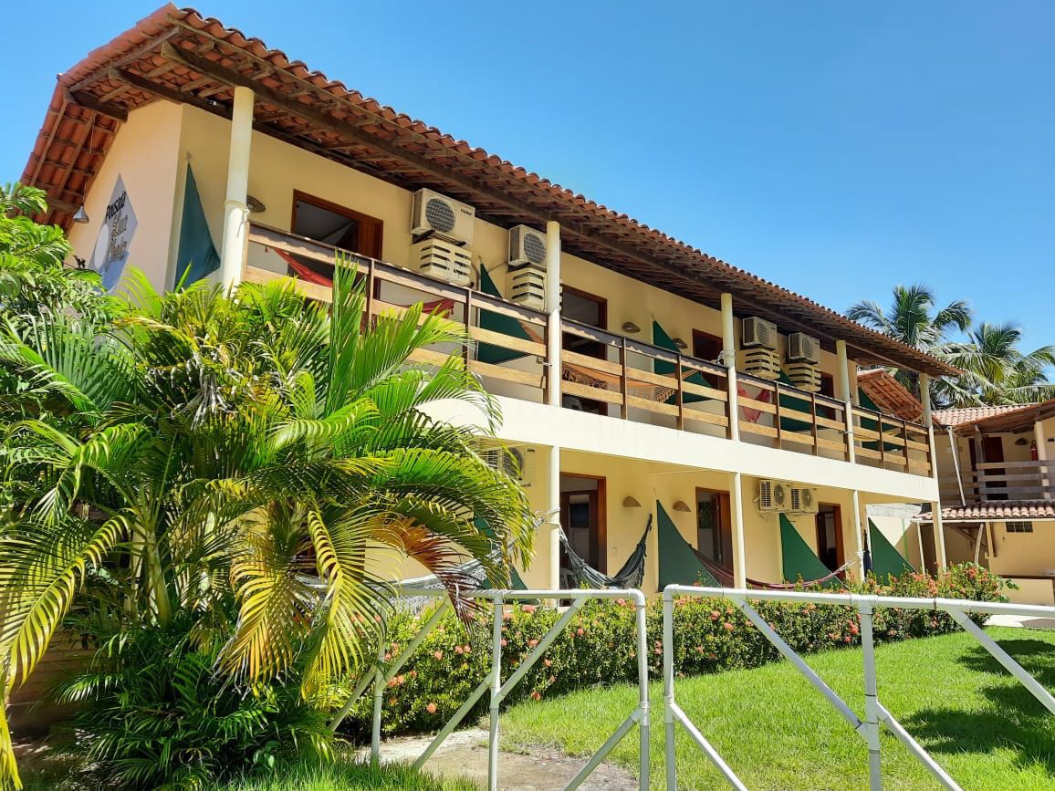 A multi-story building with balconies, air conditioning units, and a garden area with palm trees.