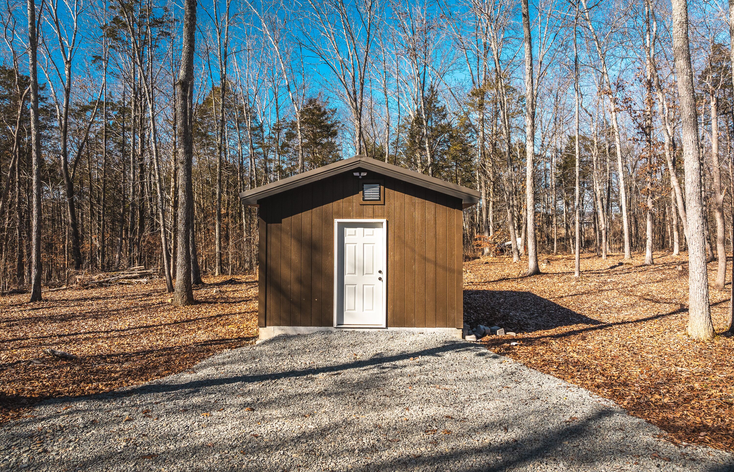 A small wooden cabin with a white door, surrounded by a forest.
