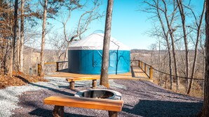 Una yurta con terraza de madera y un brasero en un área boscosa.