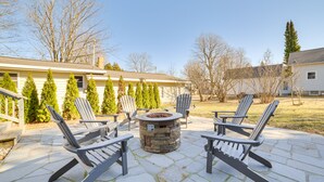 Un patio con sillas Adirondack, un hogar de fuego de piedra y piso de piedra.