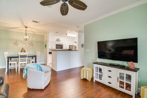 A modern living room with a flat-screen TV, a dining area with a table and chairs, and a kitchen in the background. - Foley Condo w/ Pool Access: 10 Mi to Gulf Shores! (Foley)