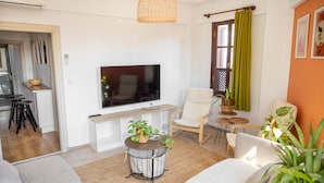 En moderne stue med et fladskærms-tv, behagelige møbler og et spisebord, der kan ses igennem en åben dør.