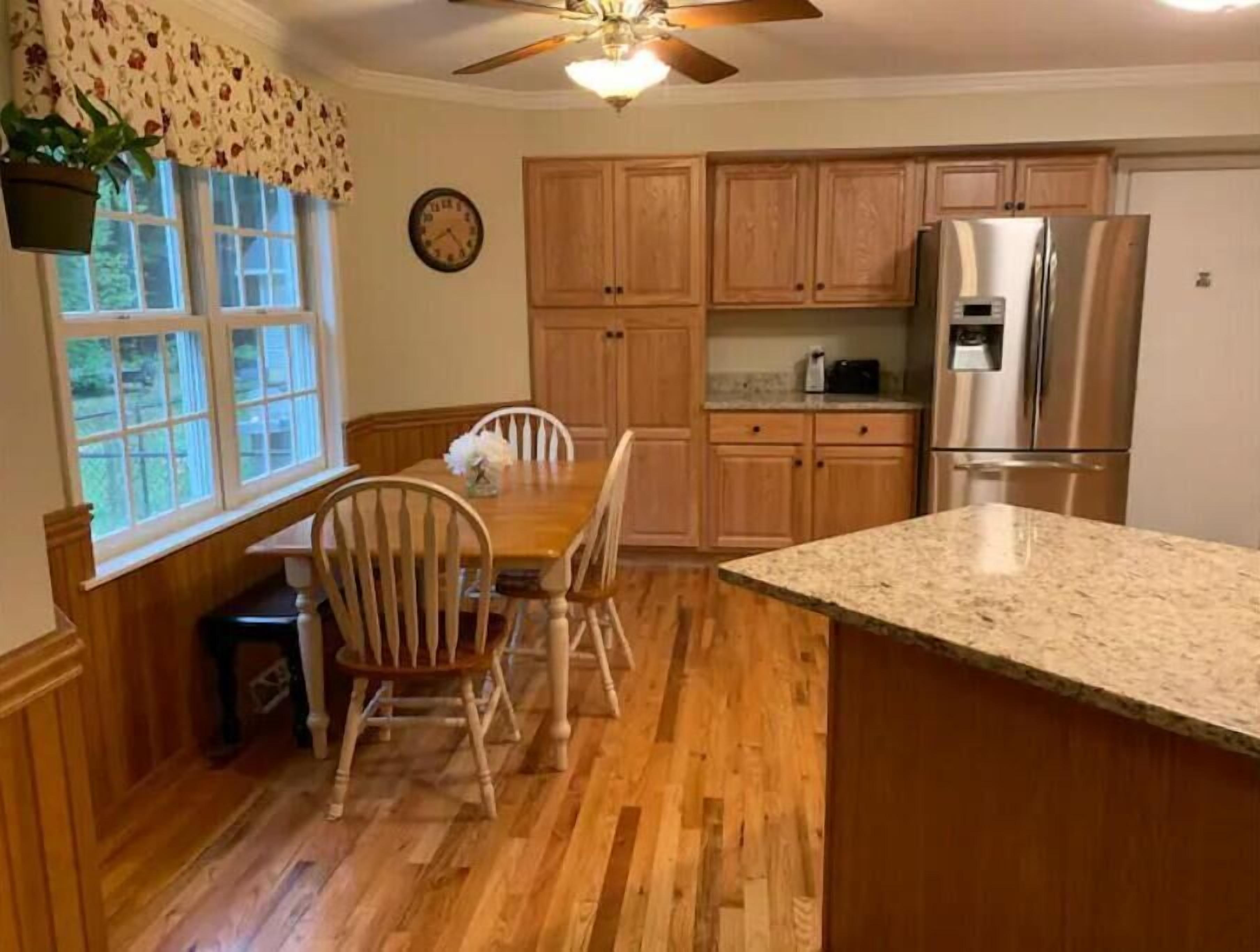 Una cocina con armarios de madera, encimera de granito, refrigerador de acero inoxidable y una mesa de comedor con sillas.