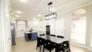 Une cuisine moderne avec des meubles blancs, un îlot central et un coin repas comprenant une table et des chaises noires.