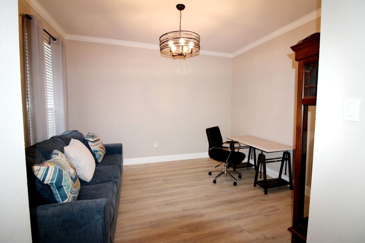 A room with a dark blue couch, a wooden dining table, a black office chair, and a hanging light fixture.