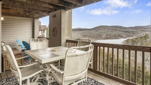 A covered outdoor patio with a table and chairs, overlooking a river and hilly landscape. - Walk-In 2BR Lakeview Condo | Near SDC (Branson)